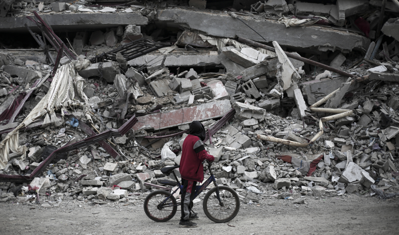 A Palestinian boy along with his bicycle looks at the rubble of a house destroyed by Israeli bombardment in Rafah in the southern Gaza Strip on February 27, 2024. (AFP)