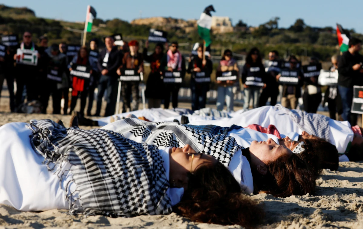 Activists wrapped in white sheets lie in the sand to highlight the death of civilians in Gaza during a symbolic protest in Mellieha, Malta. (REUTERS)