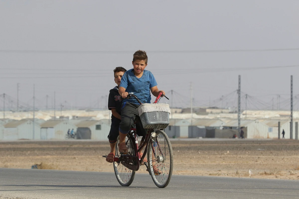 Young Syrian refugees ride a bicycle at the Azraq camp for Syrian refugees in northern Jordan on August 2, 2018. (File/AFP)