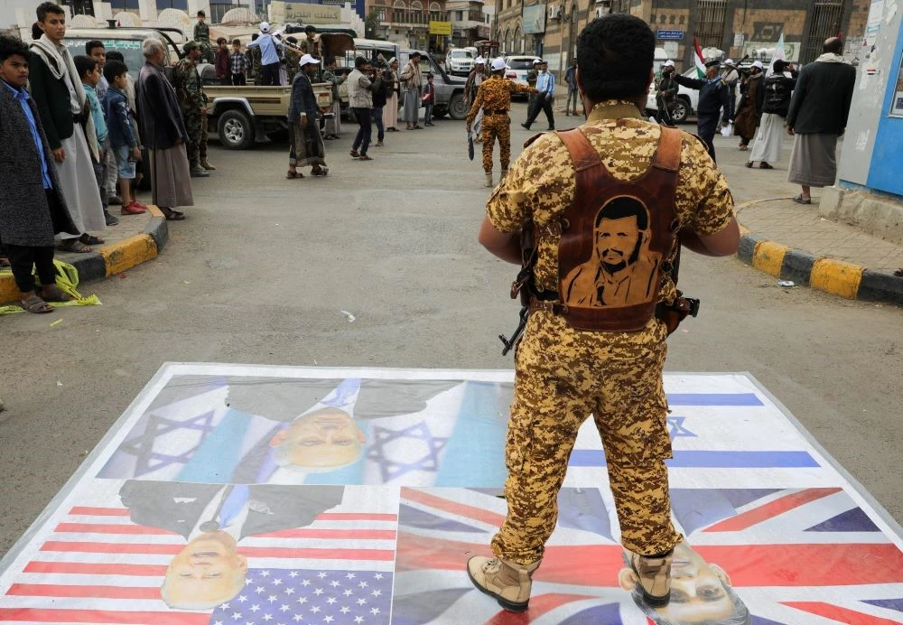 A Houthi policeman stands on a banner featuring images of Benjamin Netanyahu, Rishi Sunak and Joe Biden, Sanaa, Yemen, Feb. 8, 2024. (Reuters)