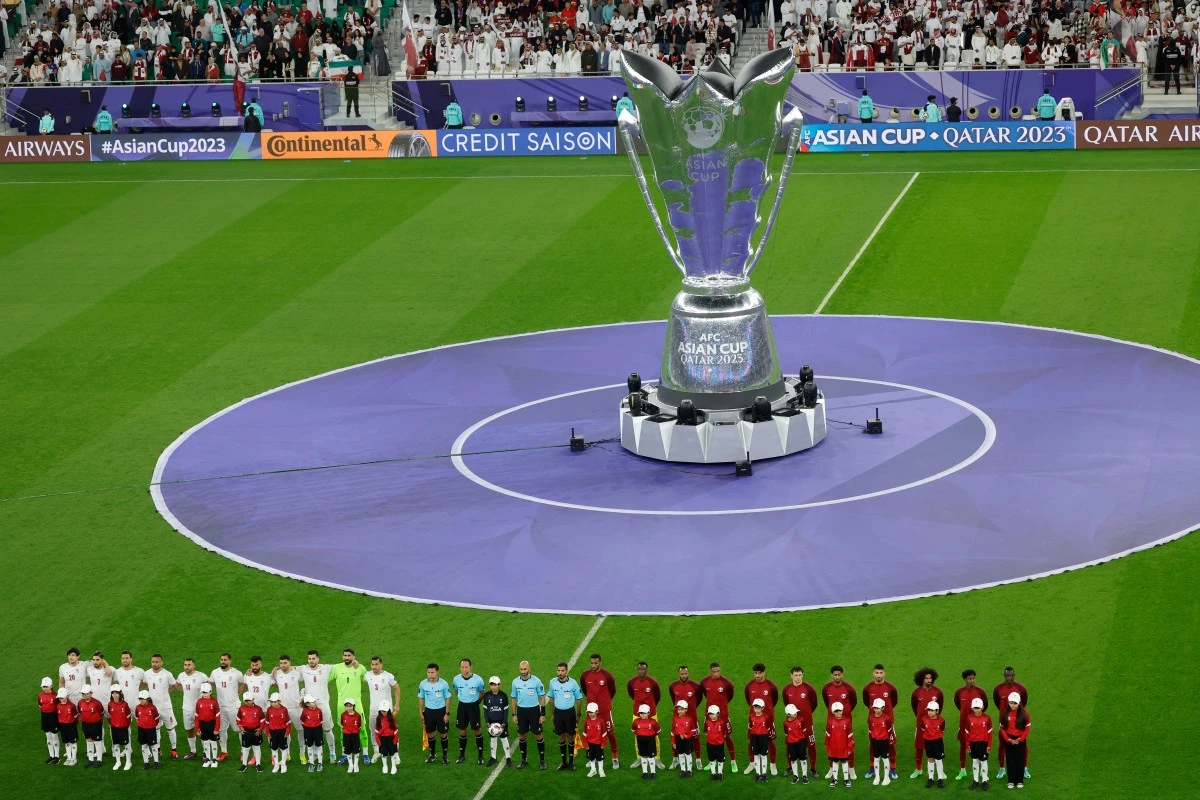 Qatar's players (R) and Iran's players line-up in front of a large-scale Qatar 2023 AFC Asian Cup trophy replica before the start of the Qatar 2023 AFC Asian Cup semi-final football match between Iran and Qatar (AFP)