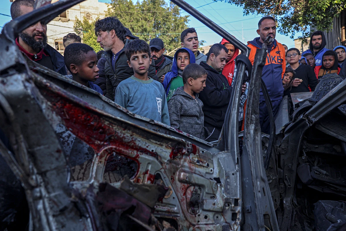 Onlookers gather around a car that was destroyed in an Israeli raid in Rafah in the southern Gaza Strip. (File/AFP)
