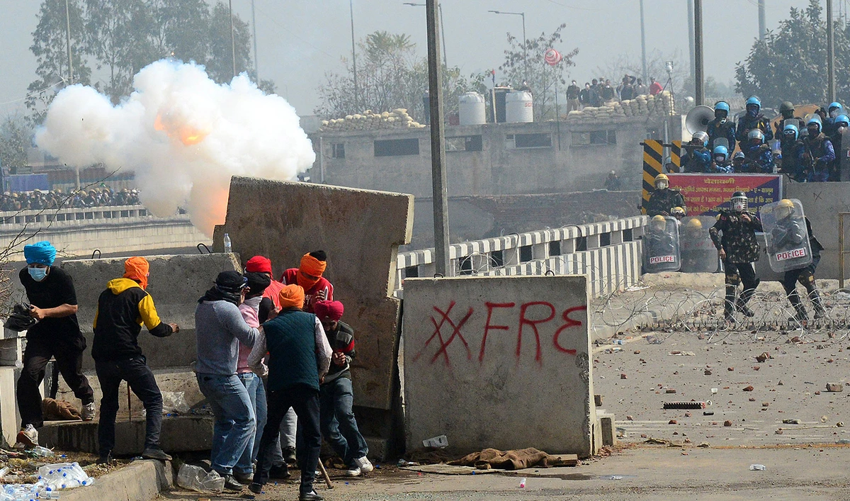 Farmers take cover behind concrete road dividers as police fire teargas to disperse farmers marching towards India's capital during a protest demanding minimum crop prices near the Haryana-Punjab state border at Shambhu in Patiala district on February 21, 2024. (AFP)