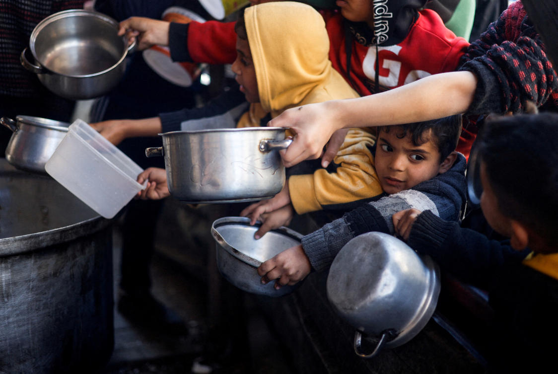 Palestinian children wait to receive food cooked by a charity kitchen amid shortages of food supplies, in Rafah, on Mar. 5, 2024. (Reuters)
