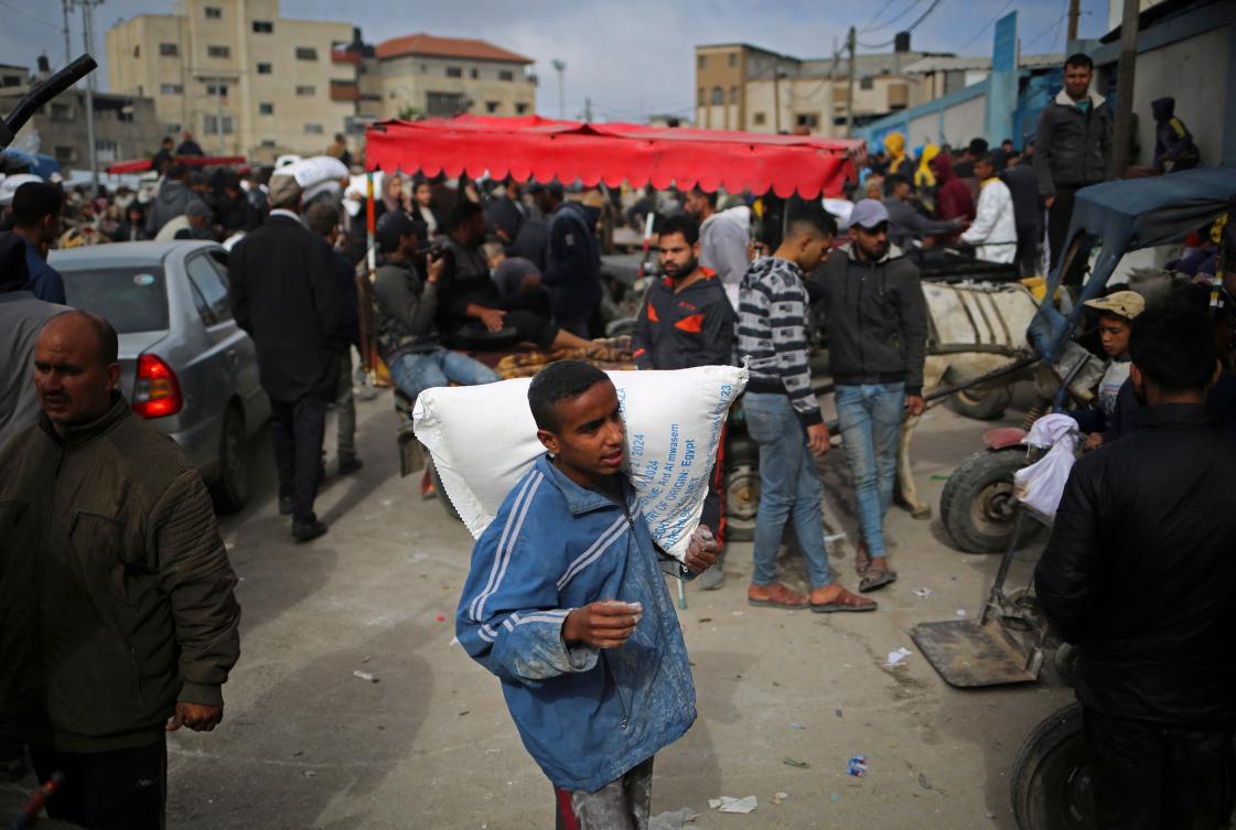 A Palestinian man carries a sack of humanitarian aid at the distribution center of UNRWA, in Rafah on Mar. 3, 2024. (AFP)