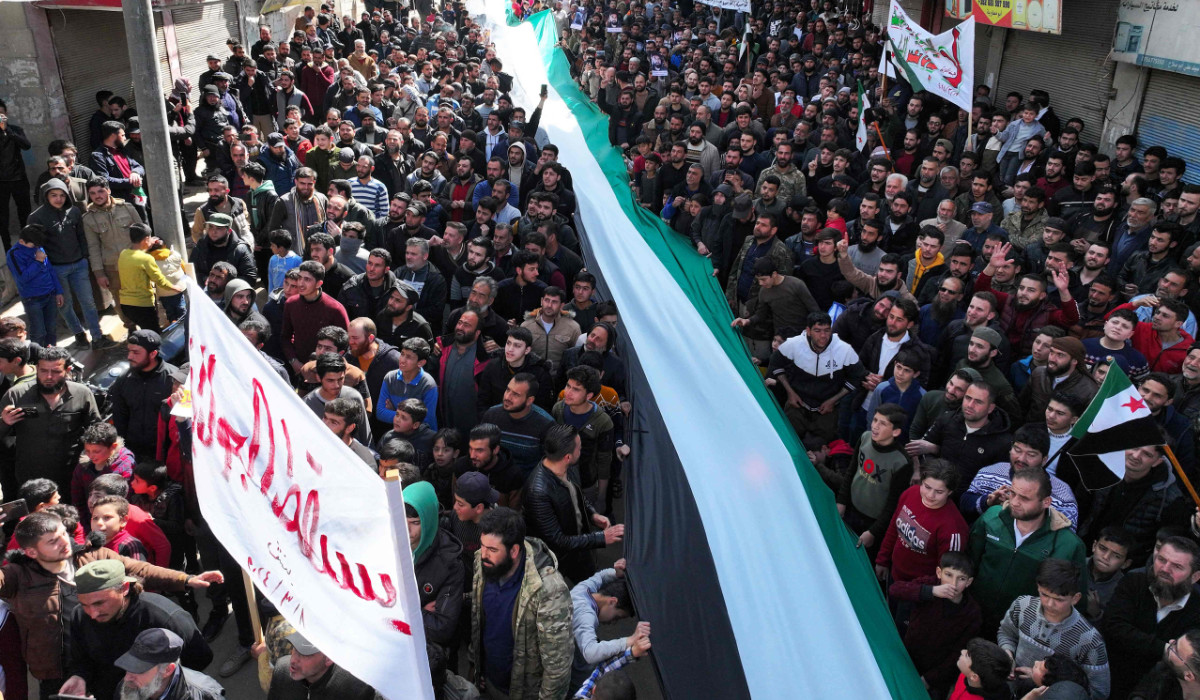 Demonstrators deploy a long opposition flag as they rally in the town of Binnish in Syria's northwestern Idlib province on March 8, 2024, to protest against Hayat Tahrir al-Sham (HTS), an Islamist group led by Al-Qaeda's former Syria branch, and calling for the overthrow of the group's leader. (AFP)