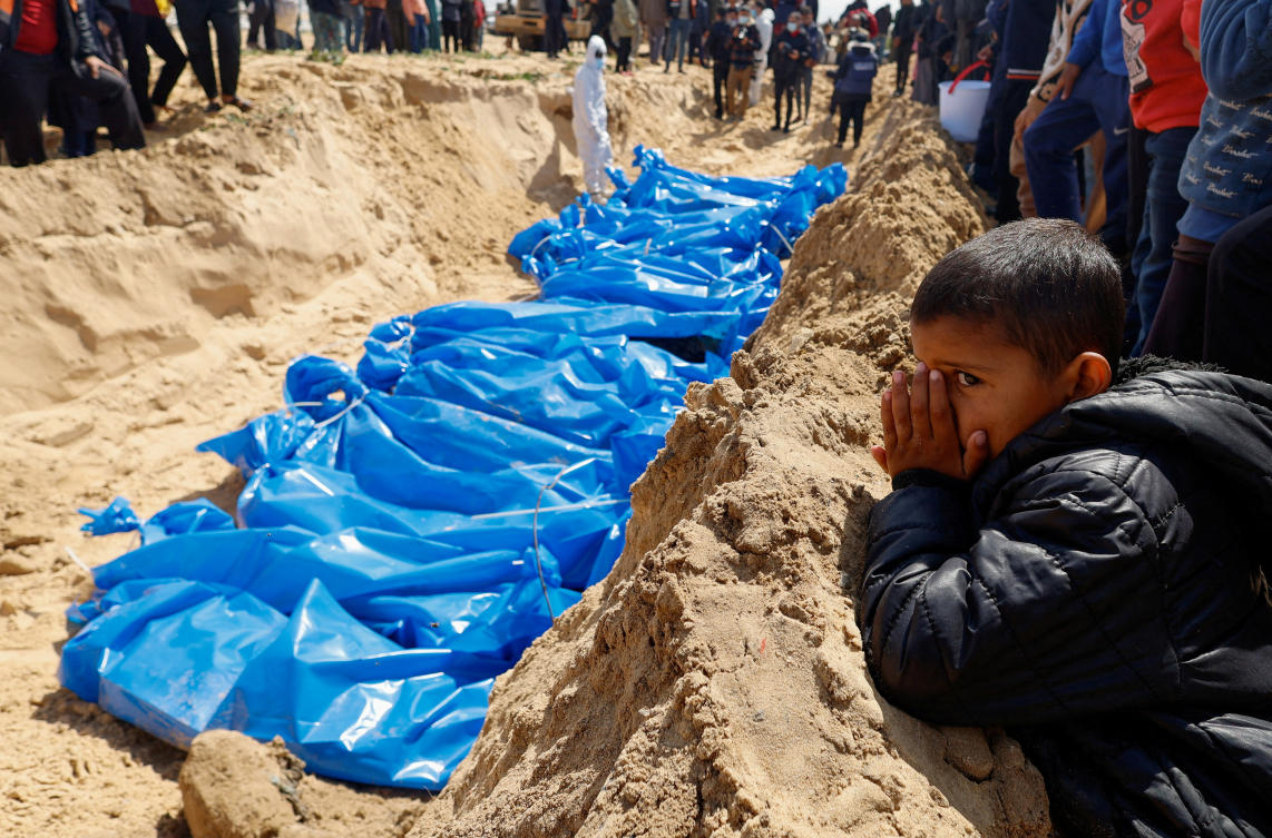 A child watches as people bury the bodies of Palestinians killed in Israeli strikes and fire, after their bodies were released by Israel, amid the ongoing conflict between Israel and the Palestinian Islamist group Hamas, at a mass grave in Rafah (REUTERS)