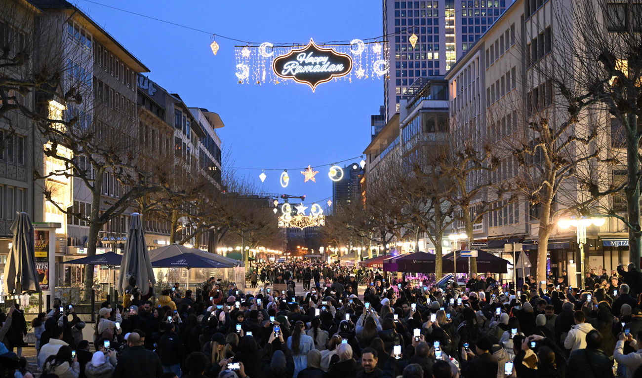 People take pictures with their mobile phones, as for the first time in Germany, on March 10, 2024 in Frankfurt, a street is illuminated during the month of Ramadan. (AFP)