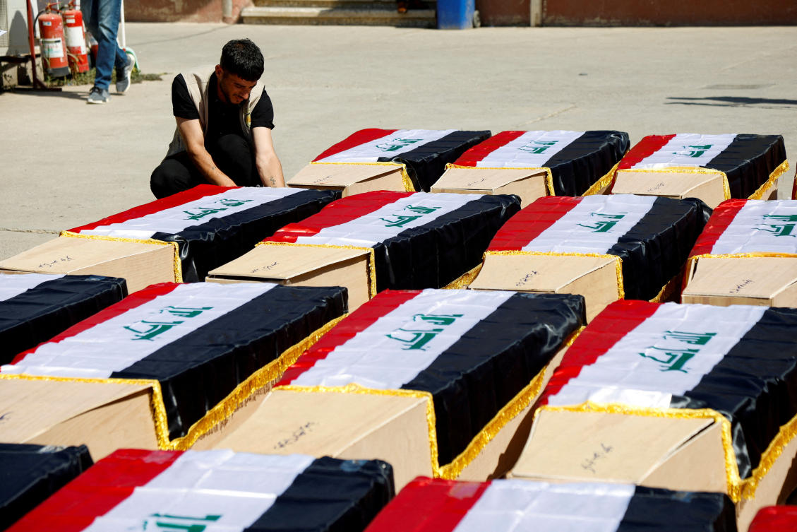 Man sits next to coffins containing remains of people from the Yazidi minority, who were killed in Daesh attacks in 2014, after they were exhumed from a mass grave, in Mosul, Iraq. (File/Reuters)