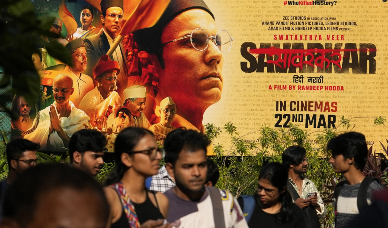 People walk past a large poster of the movie Swatantra Veer Savarkar displayed outside a cinema hall in Mumbai, on March 21, 2024. (AP)