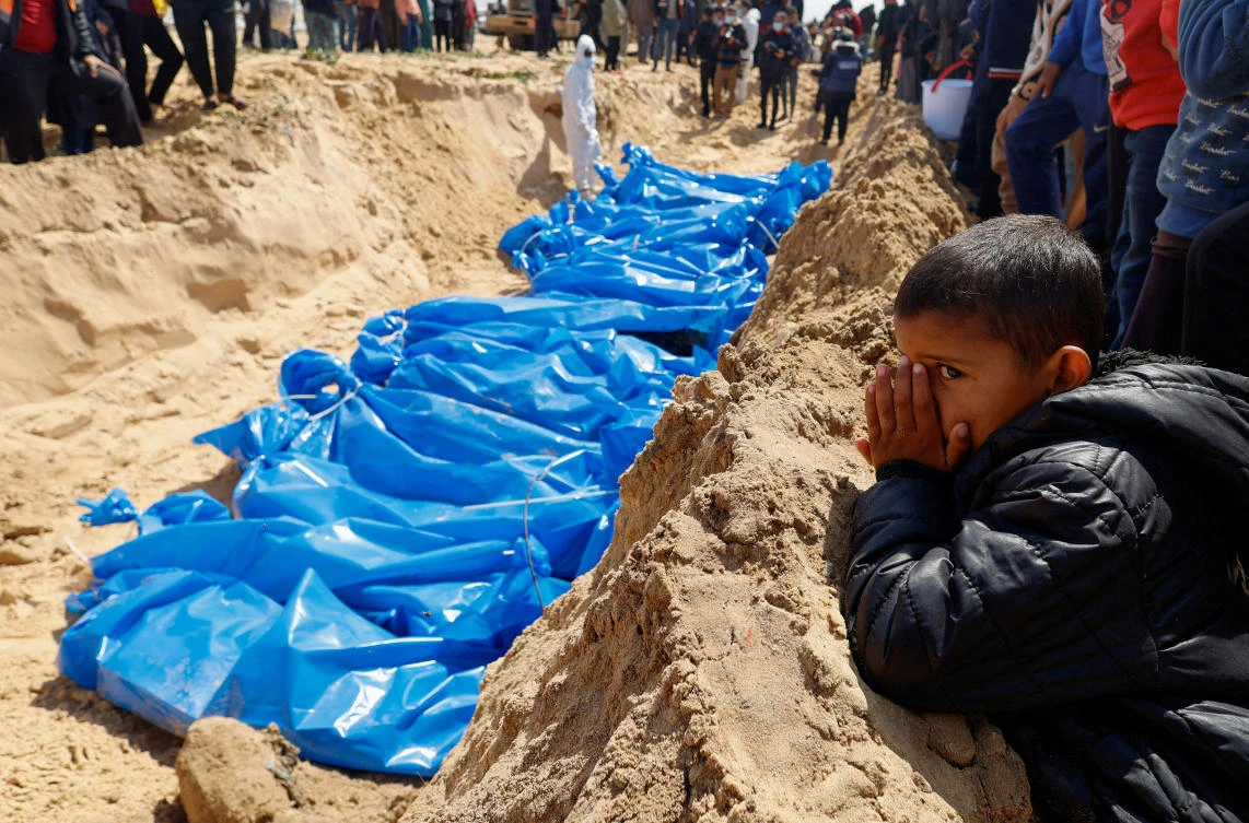 A child watches as people bury the bodies of Palestinians killed in Israeli strikes and fire, after their bodies were released by Israel, amid the ongoing conflict between Israel and the Palestinian Islamist group Hamas, at a mass grave in Rafah (REUTERS)