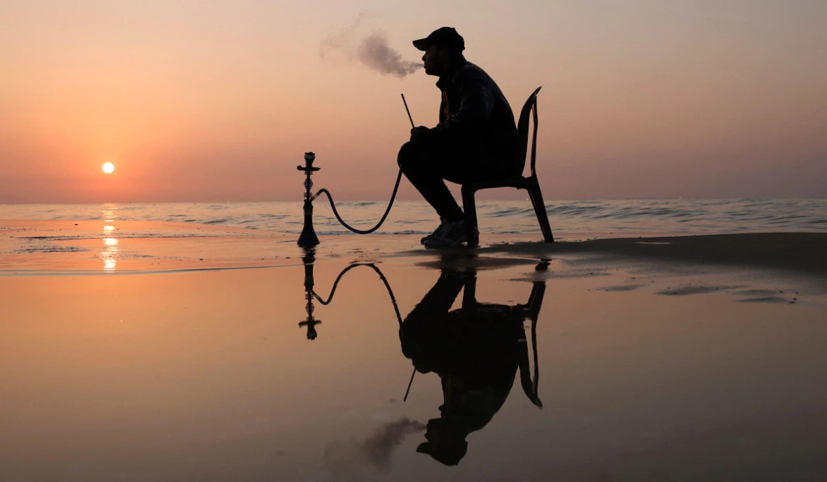 A Palestinian man smokes shisha on the beach during the last sunset of 2022, in Gaza City, on December 31, 2022. (AFP)