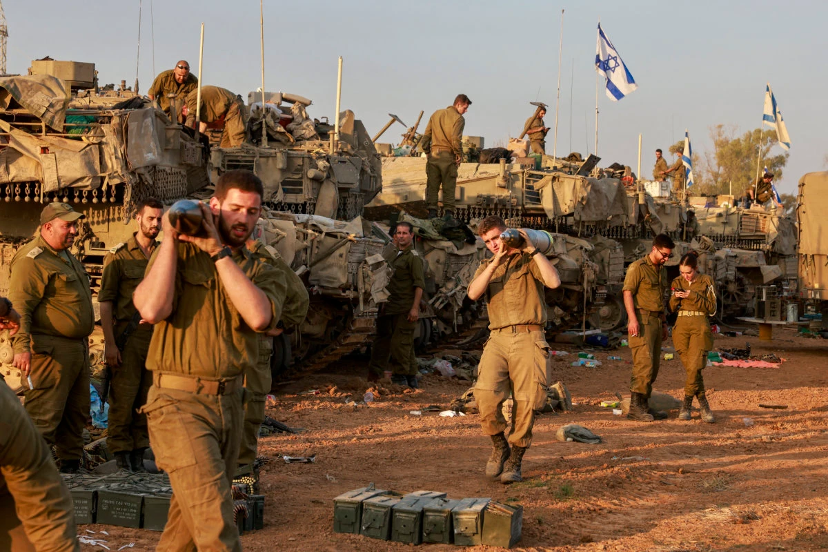 Israeli soldiers carry heavy shells past battle tanks deployed at a position along the border with the Gaza Strip and southern Israel as they pursue Hamas militants in Gaza. (AFP)