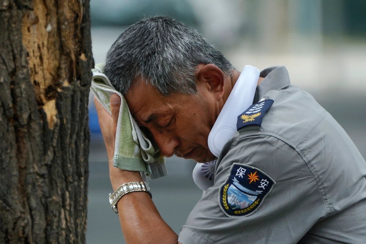 A security guard wearing an electric fan on his neck wipes his sweat on a hot day in Beijing on July 3, 2023. (AP Photo/File)