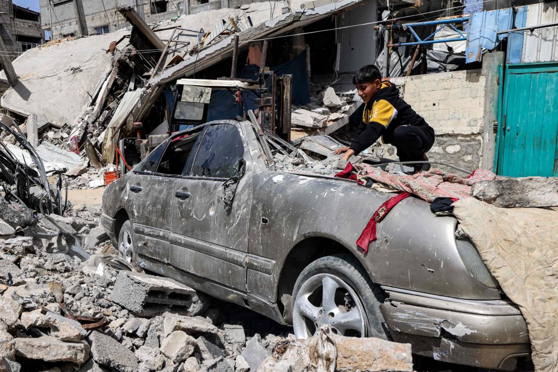 A boy clears rubble from atop a heavily damaged vehicle outside a destroyed building in Rafah in Gaza on Apr. 5, 2024. (AFP)