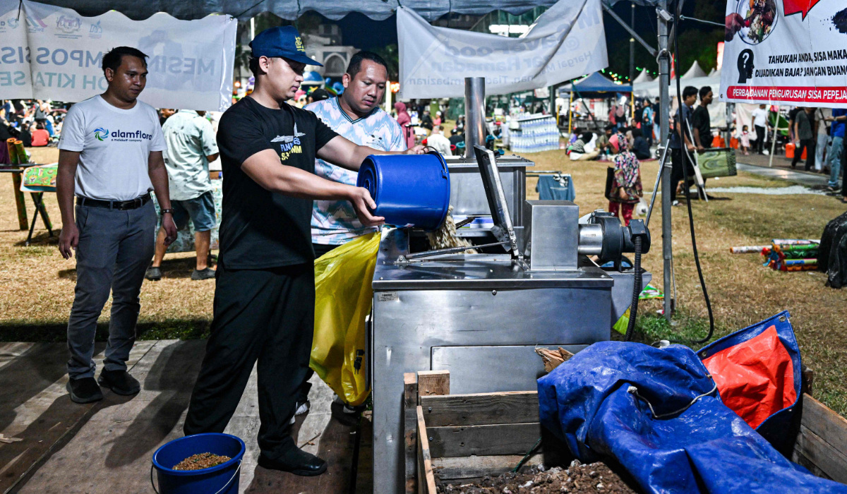 This picture taken on April 3, 2024 shows a Ramadan bazaar trader throwing food waste into a composting machine in Kuantan, Malaysia's Pahang state. After breaking their Ramadan fast outside a mosque in Malaysia, people throw their leftovers into a machine that converts the food scraps into organic fertiliser for crops. (AFP)