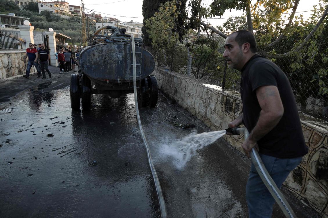 Men clean the reported site of an Israeli strike on vehicles in the southern Lebanese village of Shehabiya on April 16, 2024. (AFP)