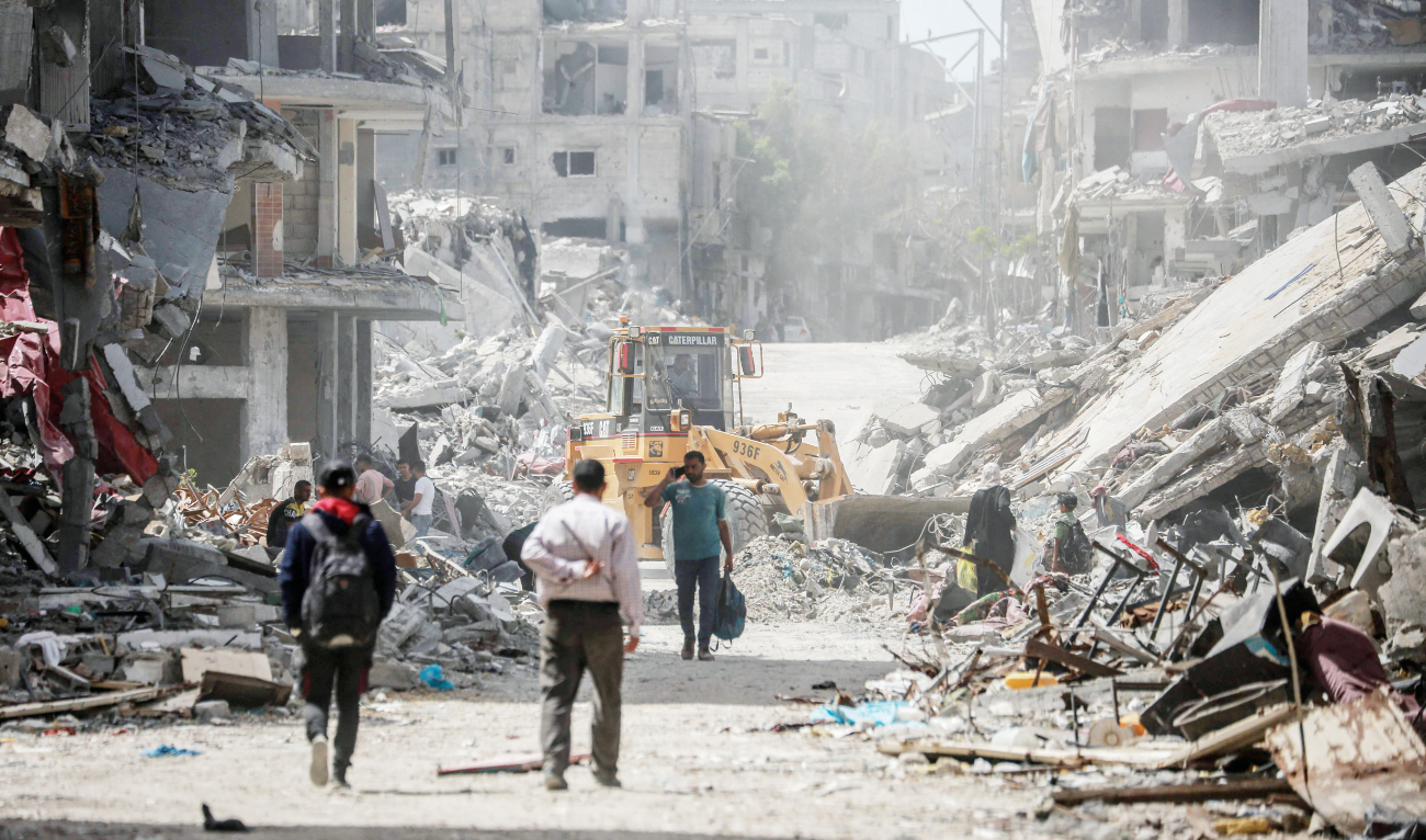 Palestinians walk on a road lined with destroyed buildings in Khan Younis in the southern Gaza Strip on Monday. (AFP)