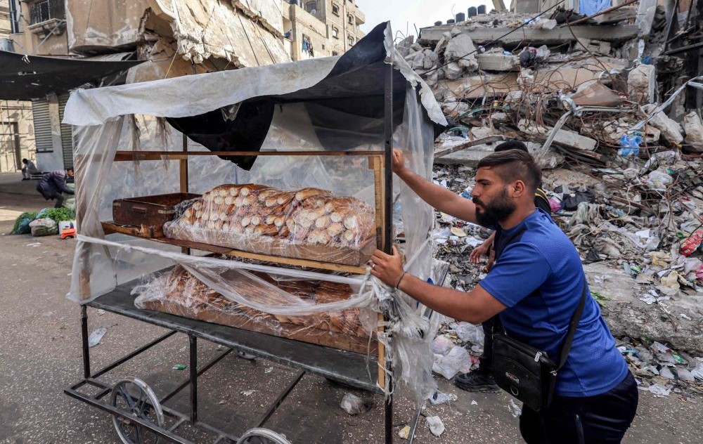 A vendor selling bread pushes his cart past the rubble of a collapsed building in Rafah, southern Gaza Strip, Apr. 23, 2024. (AFP)