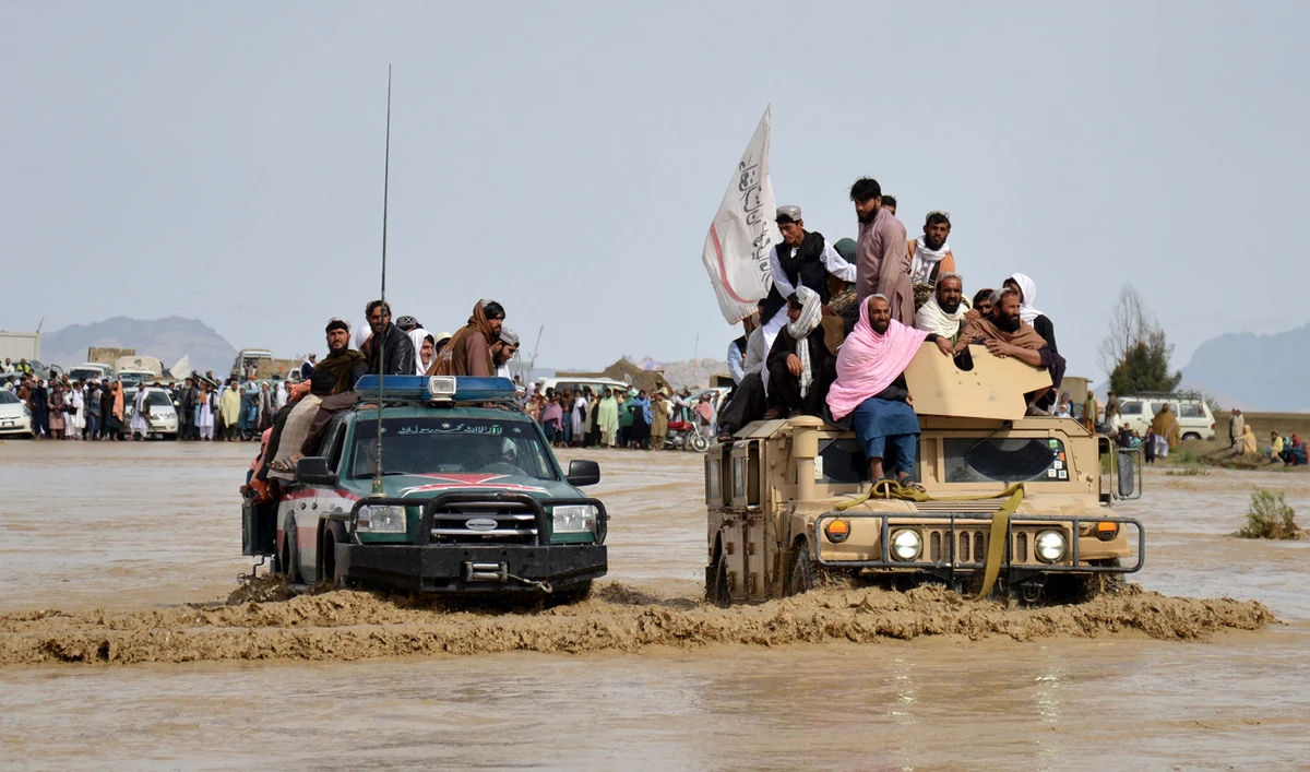 Afghan men sit atop of military vehicles as they cross through a flooded area in Spin Boldak district of Kandahar province on April 13, 2024, after a flash flood following a heavy rainfall. (AFP)