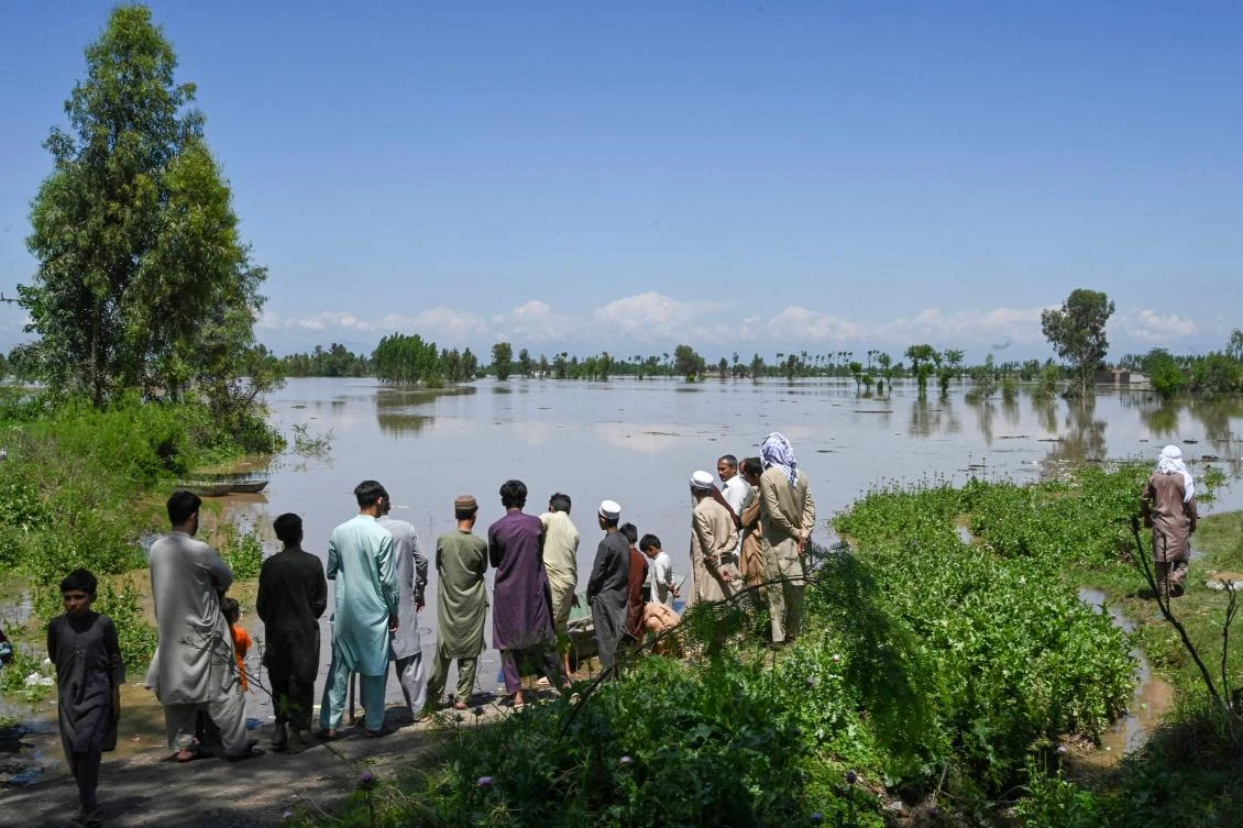 People stand on the banks of a flooded area after heavy rains in Nowshera district, Khyber-Pakhtunkhwa province (AFP)