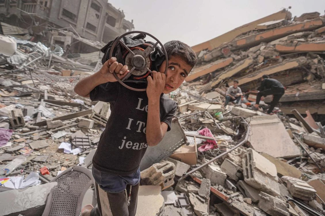 A Palestinian carries a gas cooker as he walks amidst the debris of a destroyed building in the city of Nuseirat in the central Gaza Strip on April 18, 2024. (AFP)