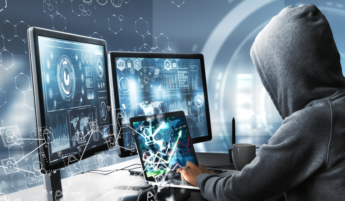 Side view of hacker using computer with digital interface while sitting at desk of blurry interior. (Shutterstock)