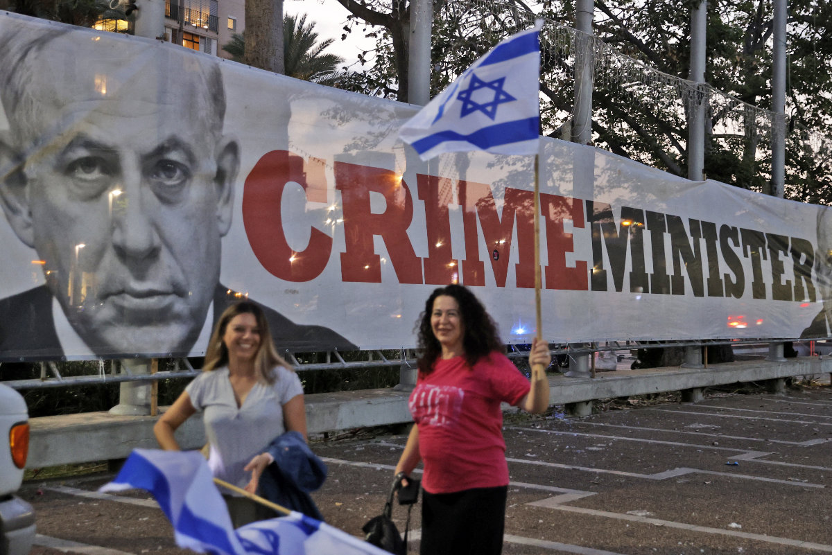Israelis walk past a protest banner against PM Benjamin Netanyahu in Tel Aviv on June 13, 2021. (AFP/File)