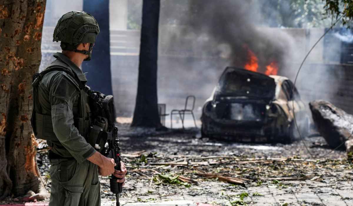 A soldier looks at a burning car at the impact site of a rocket that was fired towards Israel from Lebanon, amid ongoing cross-border hostilities between Hezbollah and Israeli forces, in Kiryat Shmona, northern Israel, May 5, 2024. (REUTERS)