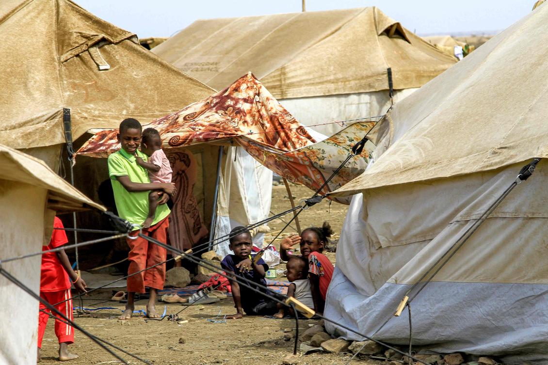 A boy carries a child as he stands next to other children sitting outside a tent at a camp for people displaced by conflict in Sudan’s eastern Gedaref province on May 15, 2024. (AFP)