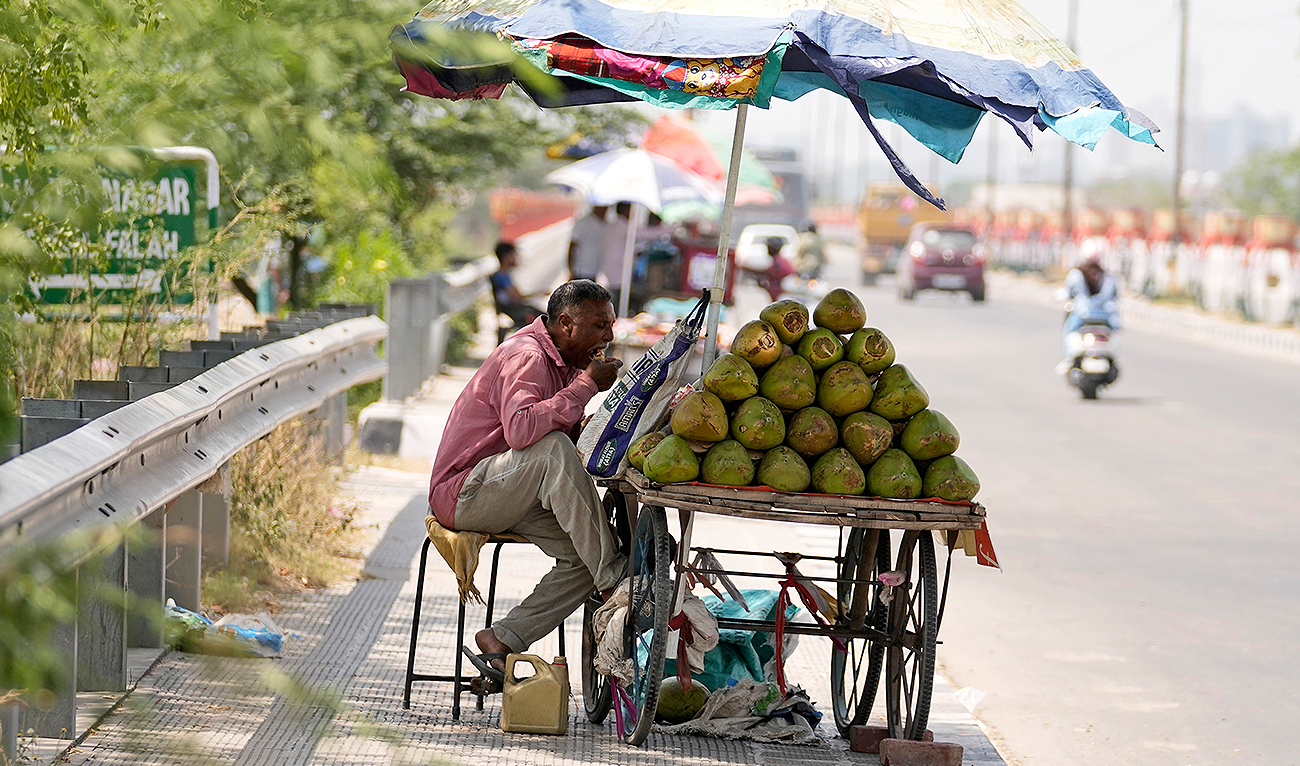 A coconut vendor eats his lunch under the shade of a beach umbrella on a hot summer afternoon in Jammu, India, Saturday, May 18, 2024. (AP)