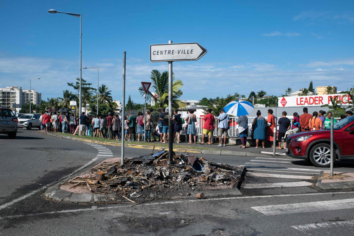 People wait in line to buy provisions from a supermarket as charred items previously set on fire are seen following overnight unrest in the Magenta district of Noumea, France's Pacific territory of New Caledonia, on May 18, 2024. (AFP)
