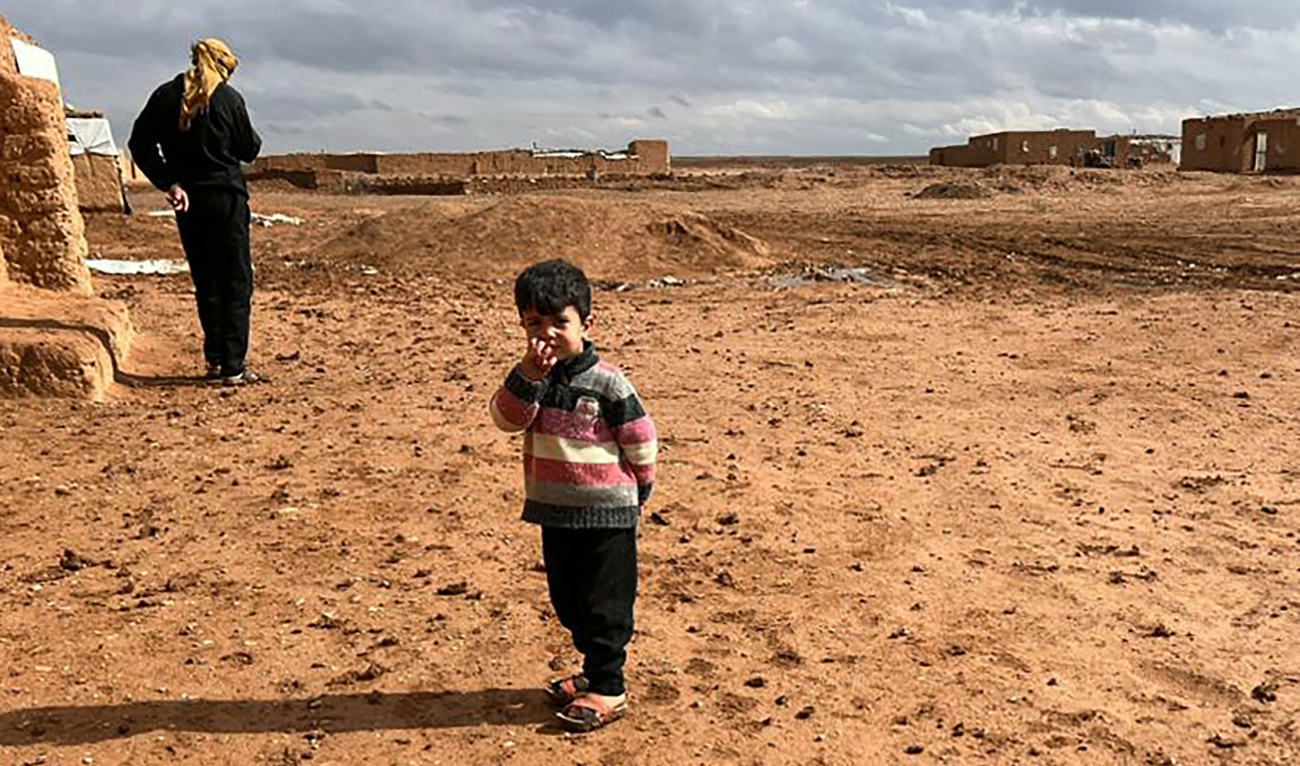 A displaced Syrian child and a man standing in front of mud houses at the Rukban camp, located in a no-man’s land in southern Syria at the border with Iraq and Jordan on May 17, 2024. (AFP)