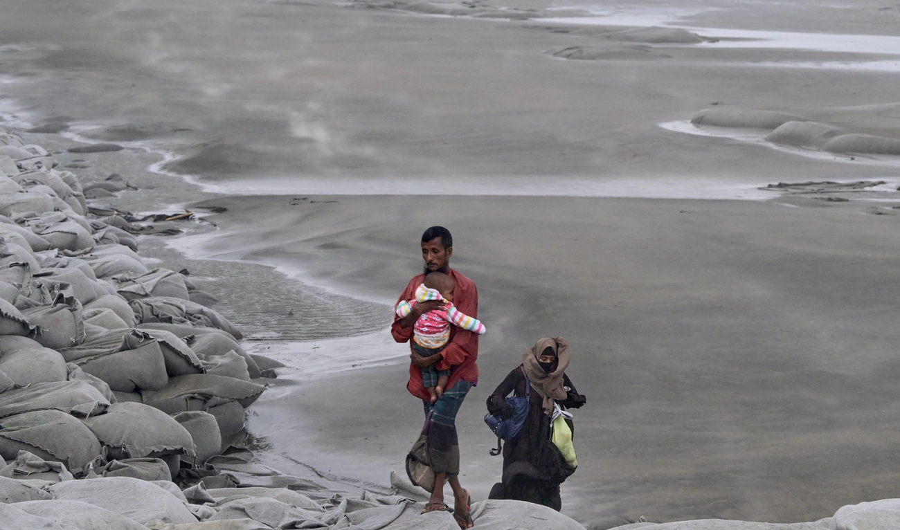 A man carries a child as he walks toward a shelter during a rainfall in Kuakata on May 26, 2024, ahead of cyclone Remal’s landfall in Bangladesh. (AFP)