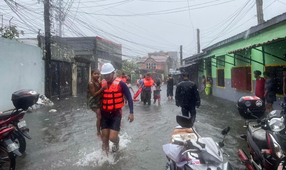 Children are evacuated from a flooded area by coast guard personnel in Lucena, Quezon Province, amid heavy rain brought by tropical storm Ewiniar. (AFP)