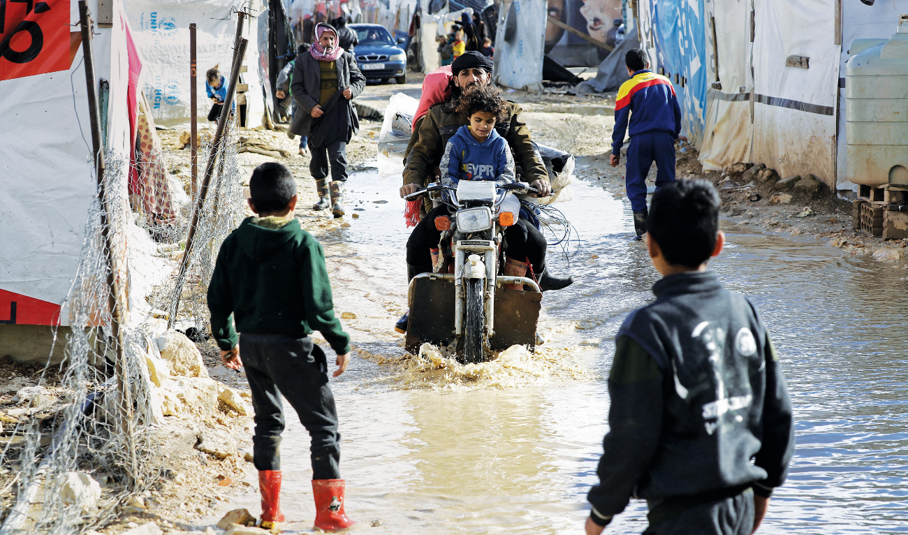 A man and his family ride on a motorbike through flood waters at an informal tent settlement housing Syrian refugees following winter storms in the area of Delhamiyeh, in the central Bekaa Valley on January 17, 2019. (AFP)