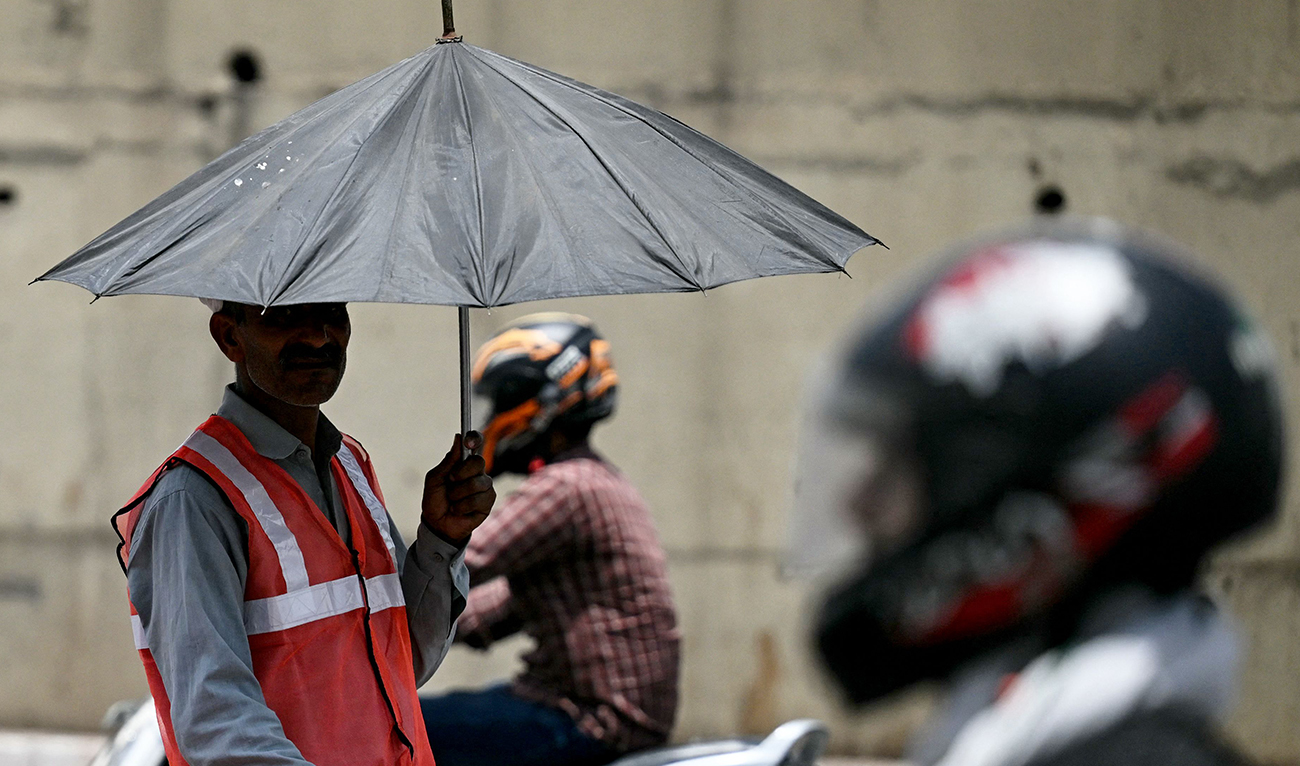 A toll booth worker (L) directing traffic takes shade under an umbrella on a hot summer afternoon in New Delhi on May 29, 2024, amid ongoing heat wave. (AFP)
