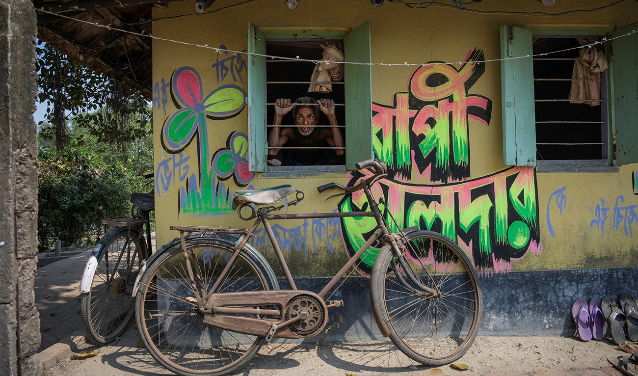 Dibakar Das, 63, looks through the window of a painted wall featuring the name of a candidate and the party symbol of the All India Trinamool Congress, a regional political party, for the ongoing general election, on Ghoramara Island in the Sundarbans, West Bengal, India, April 13, 2024. (Reuters)