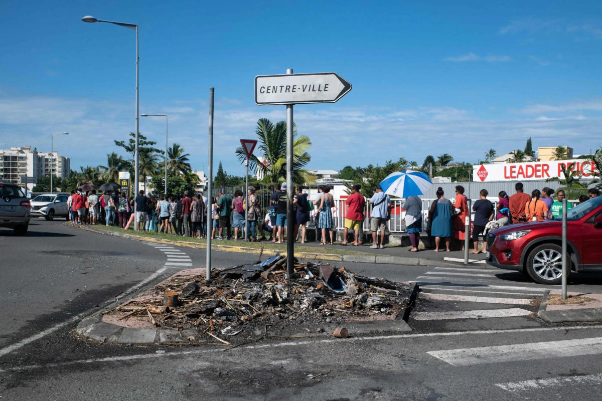People wait in line to buy provisions from a supermarket as charred items previously set on fire are seen following overnight unrest in the Magenta district of Noumea, France's Pacific territory of New Caledonia, on May 18, 2024. (AFP)