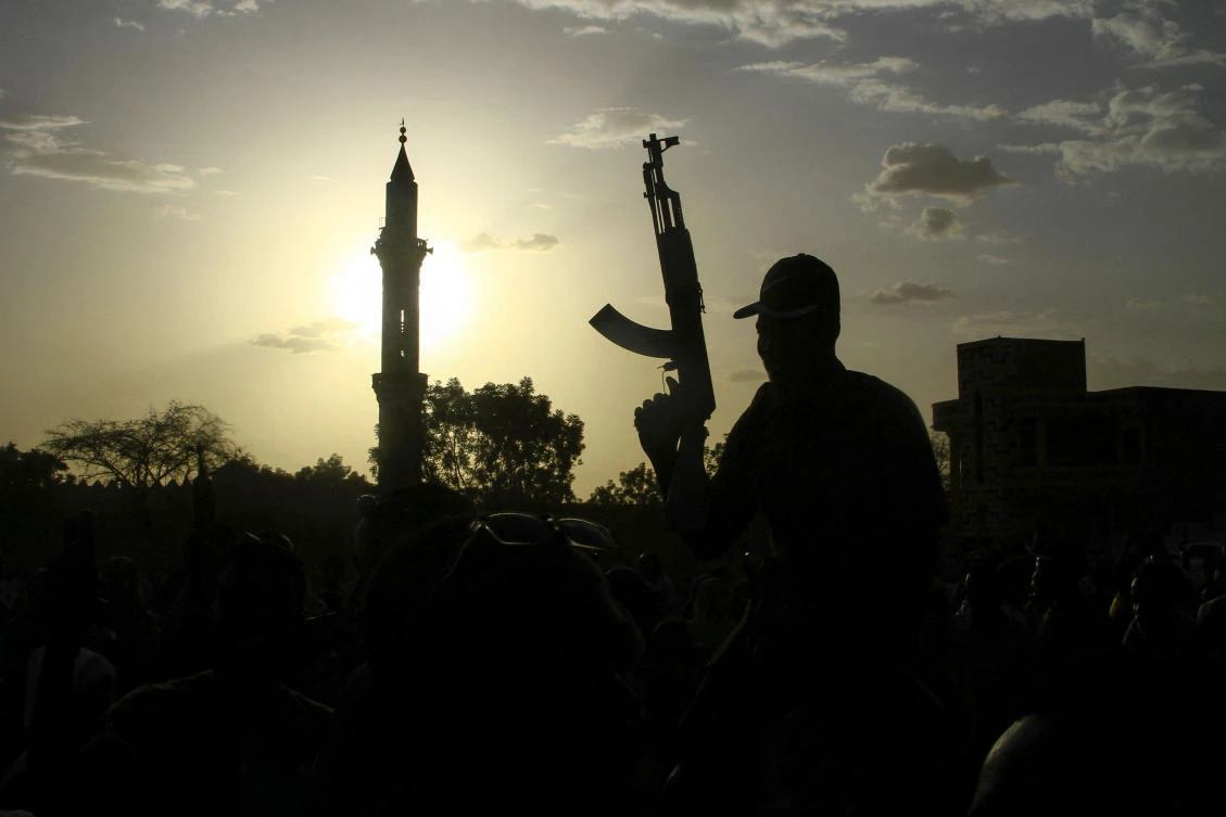 A fighter loyal to Sudan’s army chief Abdel Fattah Al-Burhan holds up a weapon backdropped by the minaret of a mosque, during a graduation ceremony in the southeastern Gedaref state on May 27, 2024. (AFP)