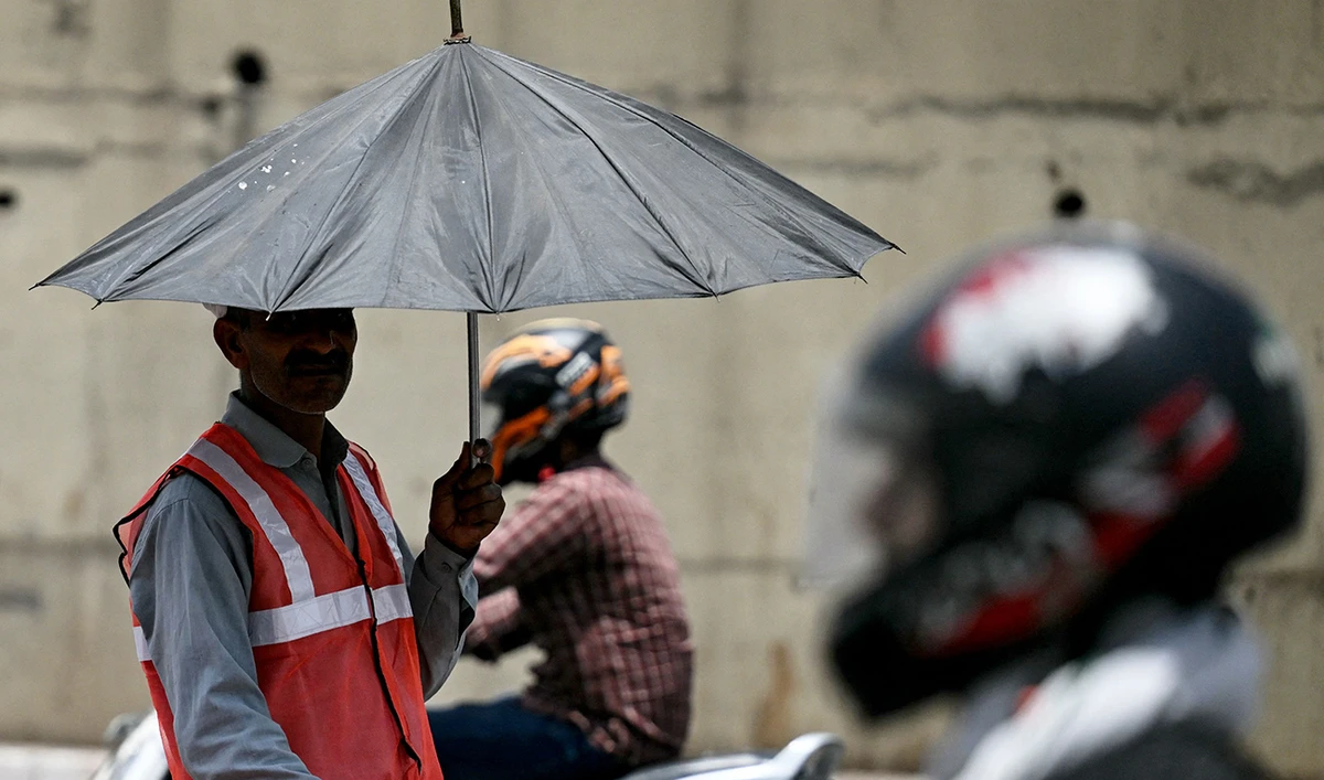 A toll booth worker (L) directing traffic takes shade under an umbrella on a hot summer afternoon in New Delhi on May 29, 2024, amid ongoing heat wave. (AFP)