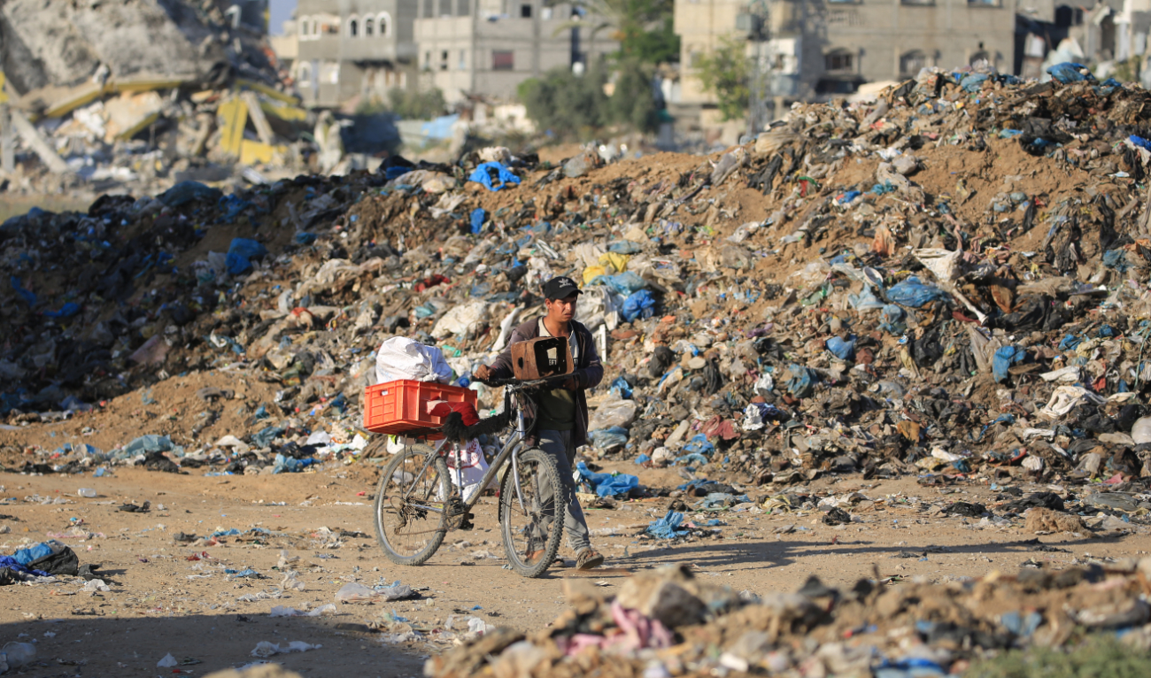 A Palestinian youth pushes a bicycle past a garbage dump at Al-Maghazi refugee camp in the central Gaza Strip on June 5, 2024. (AFP)