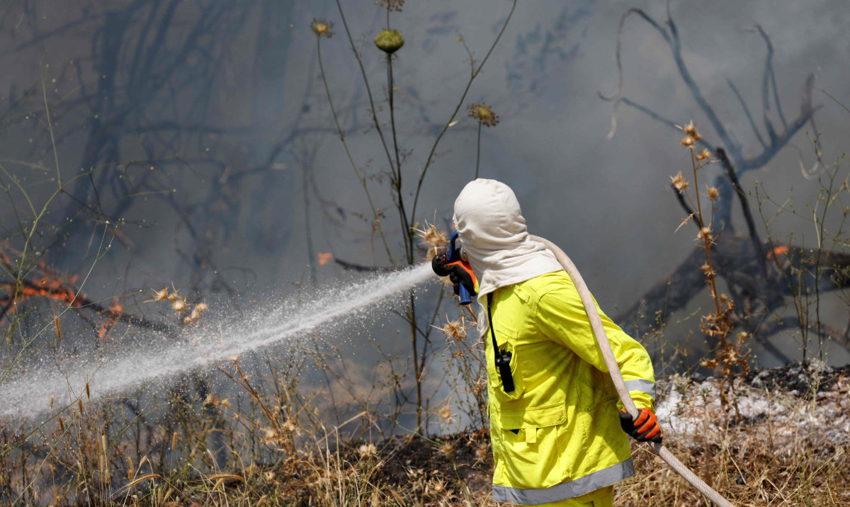 An Israeli firefighter puts out flames in a field after rockets launched from southern Lebanon landed on Banias area in the Israel-annexed Golan Heights on June 9, 2024, amid ongoing cross-border clashes between Israeli troops and Hezbollah fighters. (AFP)
