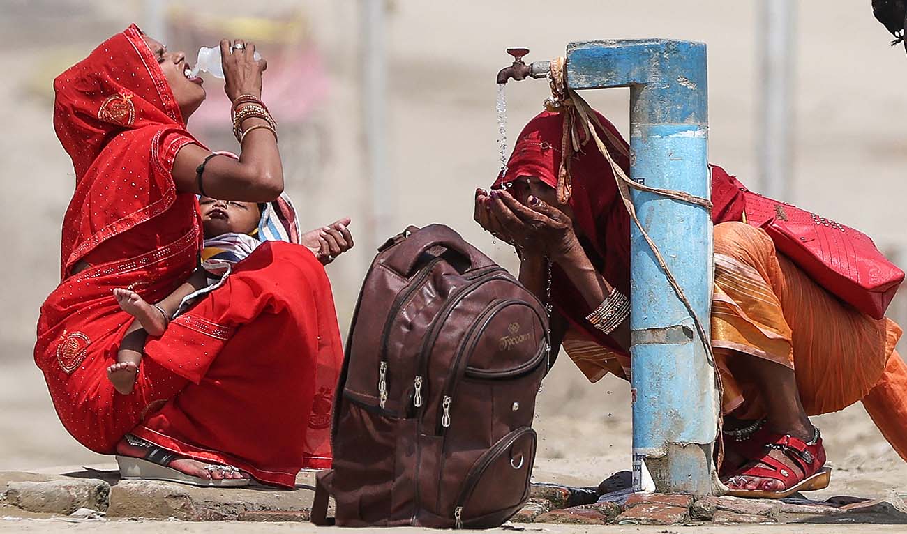 Women quench their thirst with the tap water on a hot summer afternoon during heatwave in Prayagraj on June 10, 2024. (AFP)