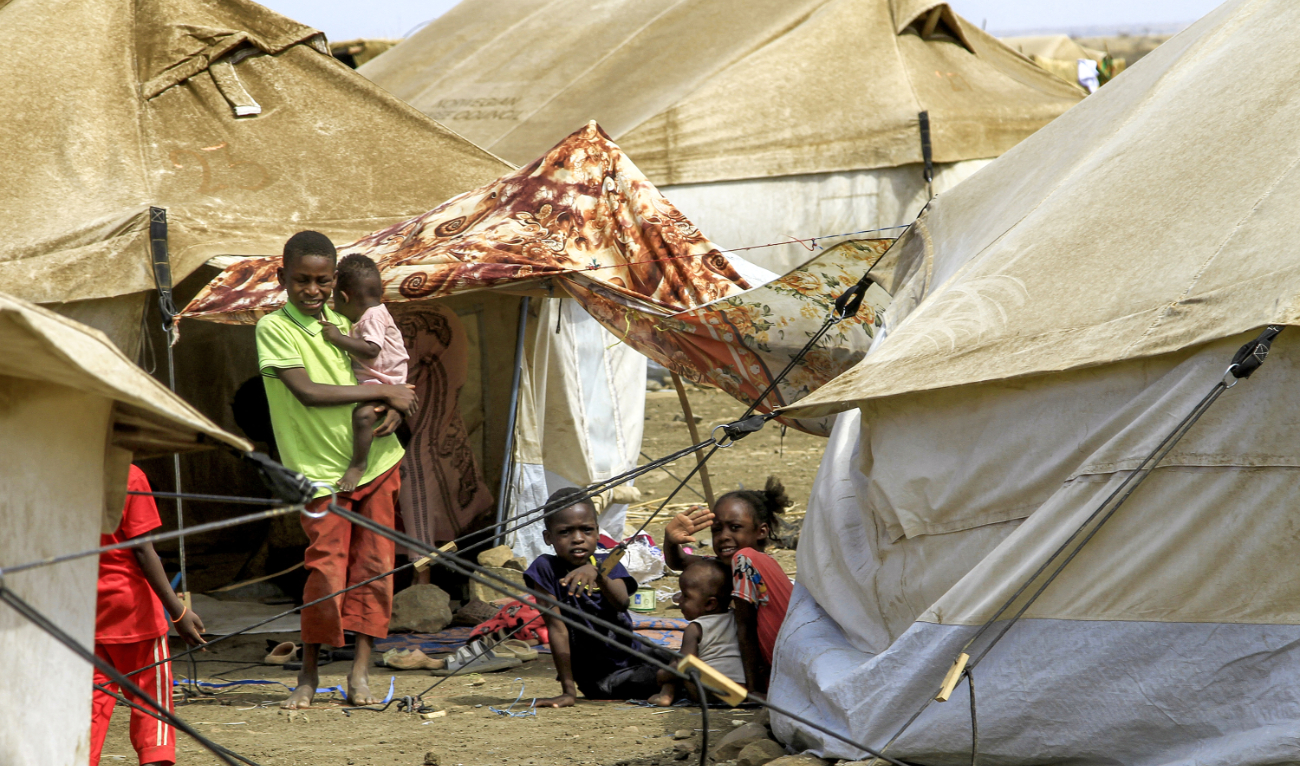 A boy carries a child as he stands next to other children sitting outside a tent at a camp for people displaced by conflict in Sudan’s eastern Gedaref province on May 15, 2024. (AFP/File)
