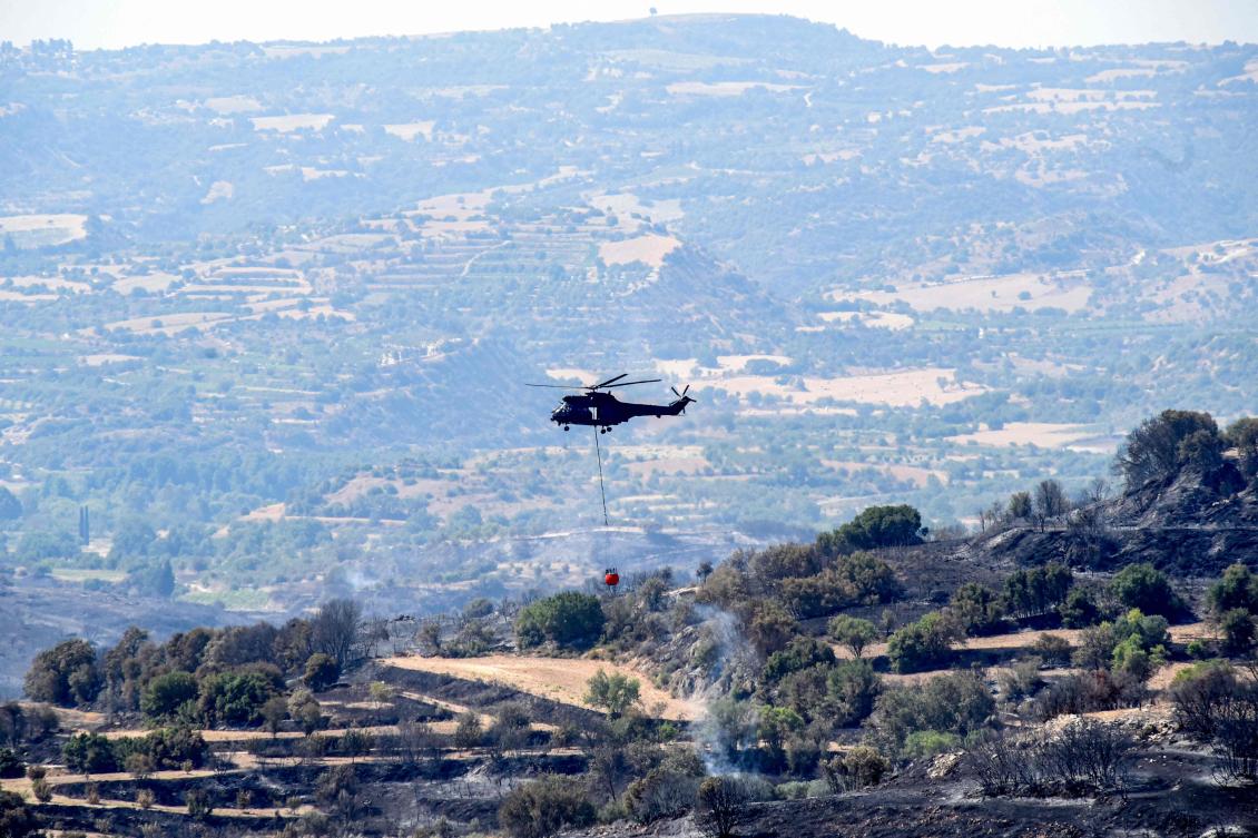 A firefighting helicopter carries a bucket while putting out a fire that broke out in Psathi in western Cyprus on June 12, 2024. (AFP)