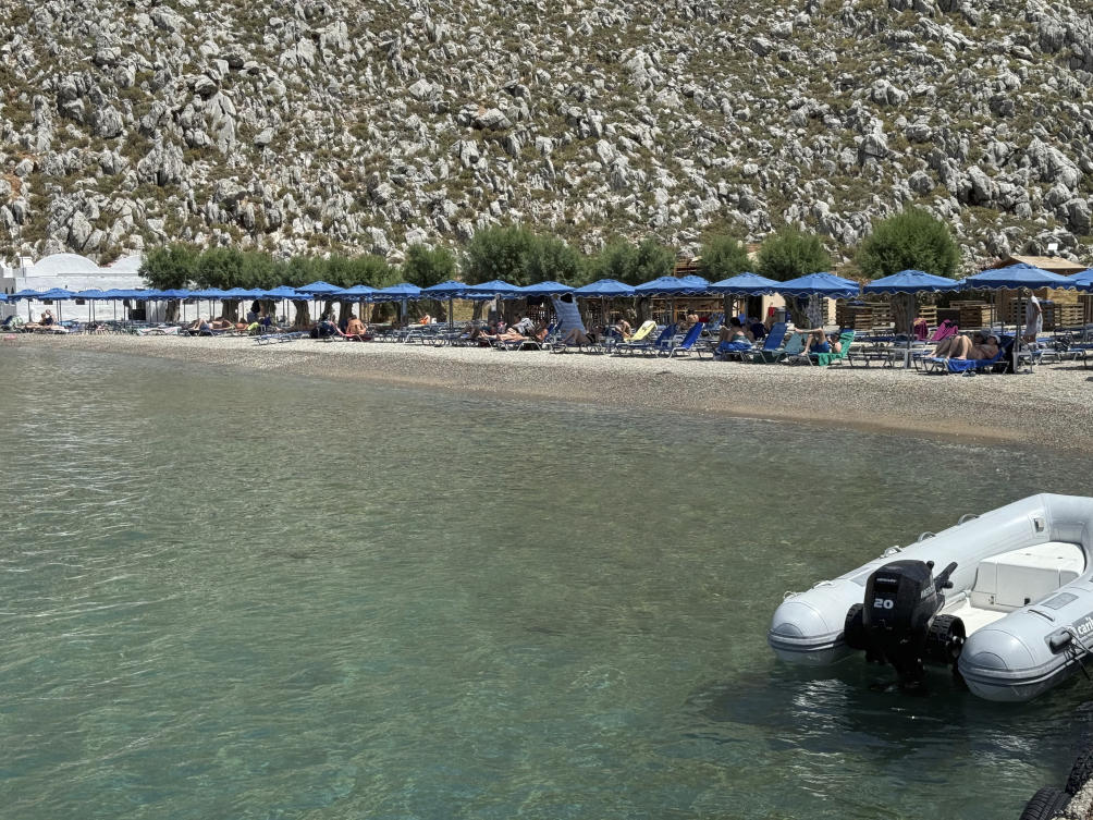 People sit on the beach of Agios Nikolaos from where British doctor and television presenter Michael Mosley, is believed to have set out, on the southeastern Aegean Sea island of Symi, Greece on Jun. 7, 2024. (AP)