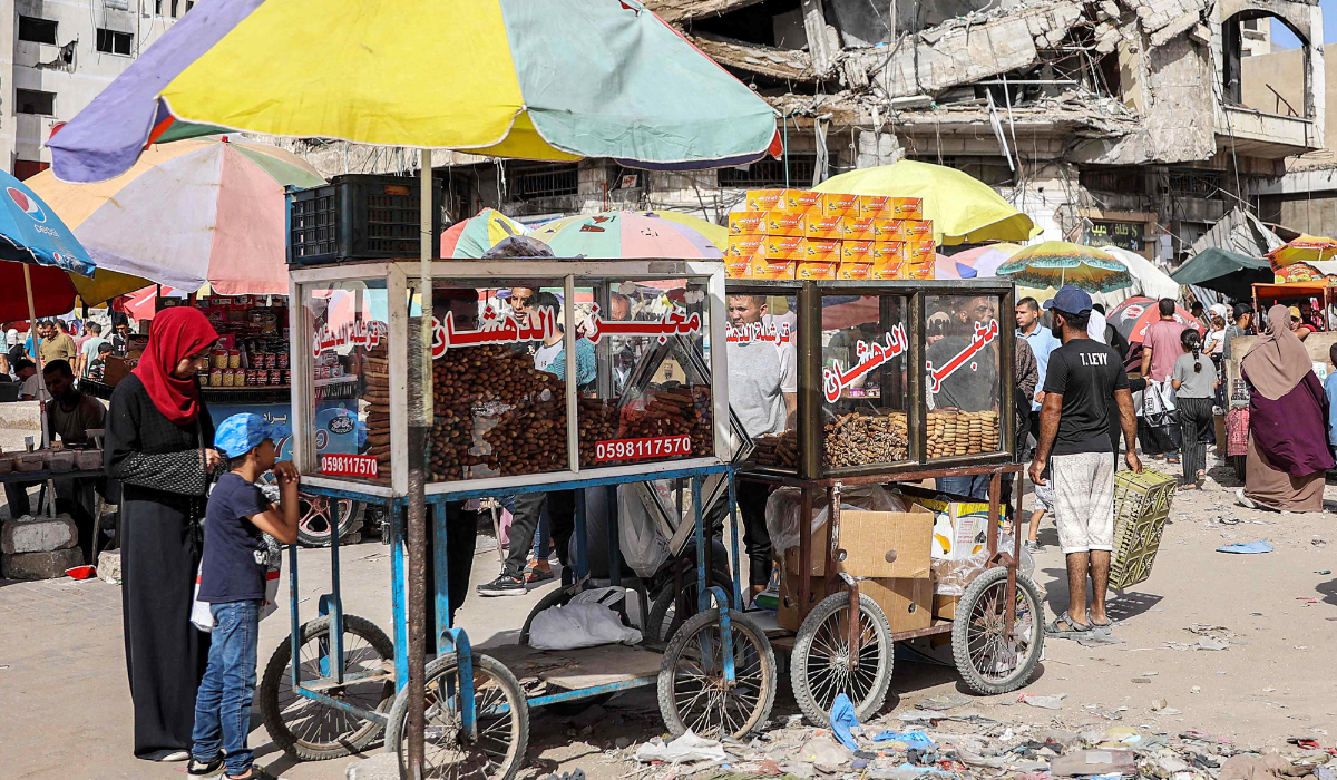 A vendor sells pastries and baked goods from his stall near a collapsed building along a market street in Gaza City on Saturday ahead of Eid Al-Adha. (AFP)