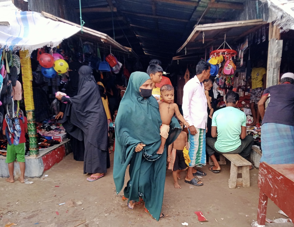 A Rohingya refugee woman carries her child as she walks through a market in Bhasan Char on June 16, 2024. (AN Photo)