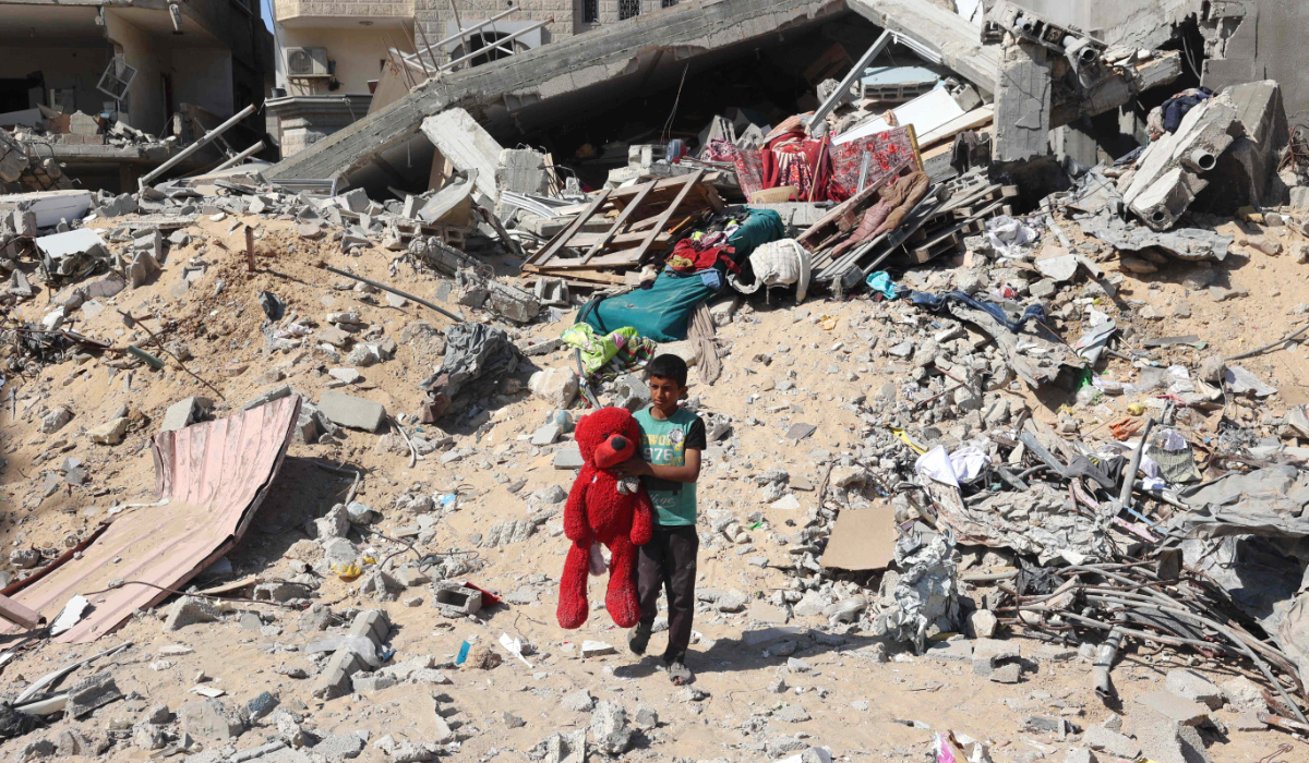 A Palestinian child walks with a stuffed bear recovered from the rubble of a destroyed building following Israeli bombardment in Khan Yunis on June 21, 2024, in the southern Gaza Strip, amid the ongoing conflict in the Palestinian territory between Israel and Hamas. (AFP)